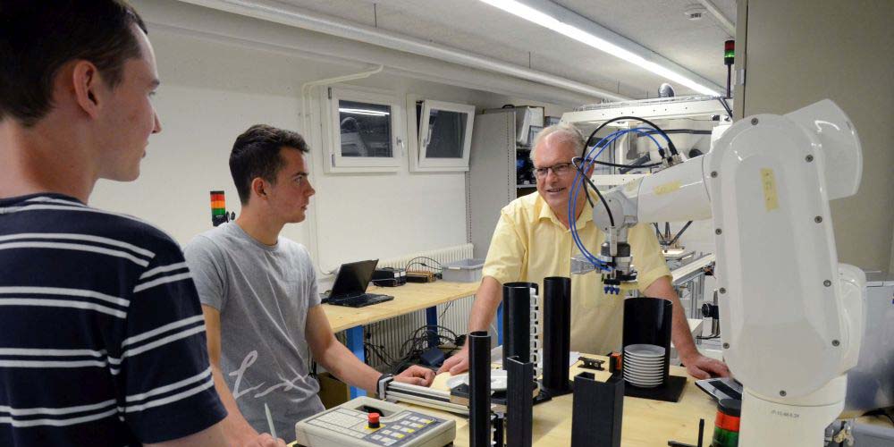 Rektor Felix Lengwiler tauscht sich mit angehenden Polymechanikern über den Kaffeeroboter aus.